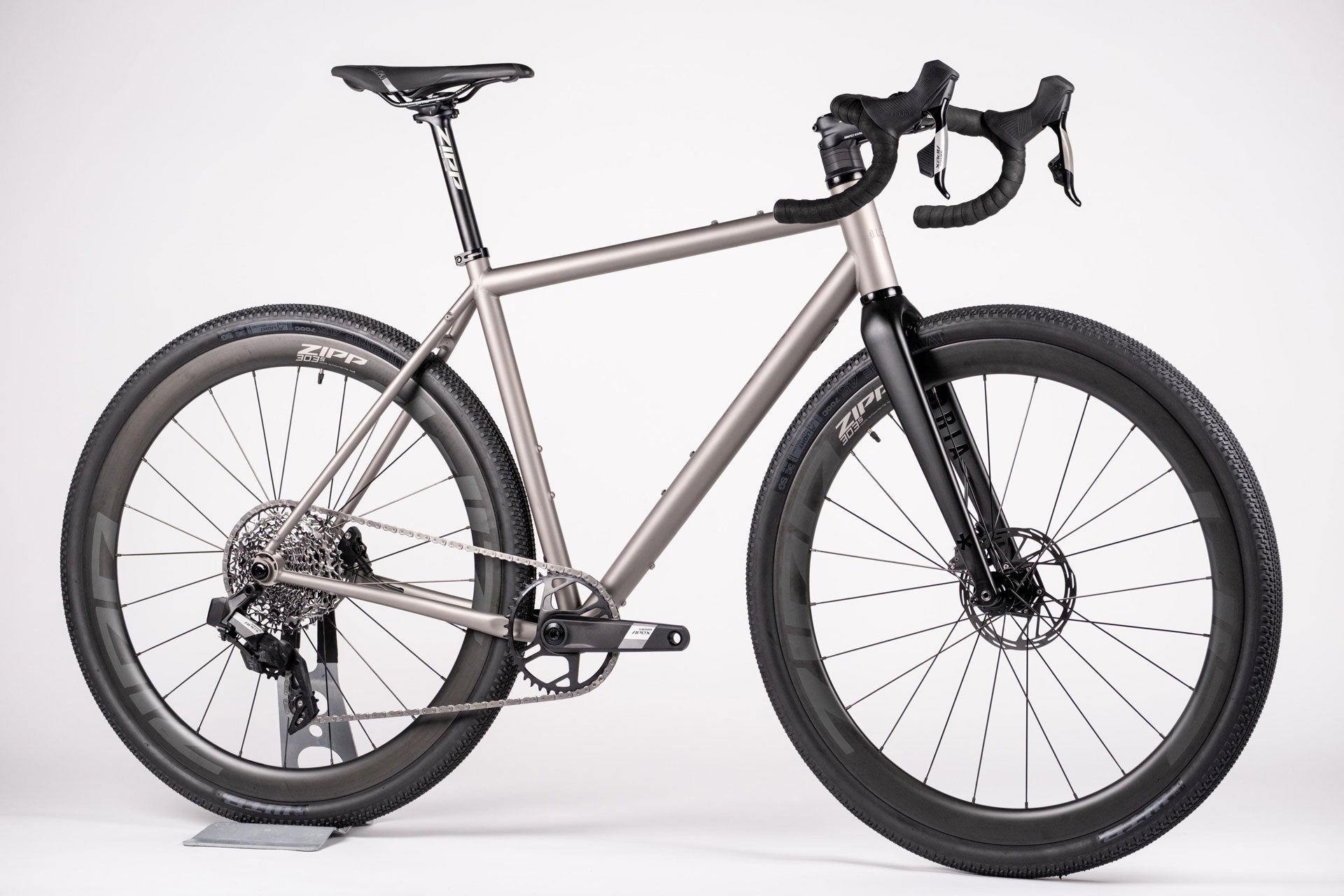 A titanium all-road bicycle with a carbon wheelset, black tires, and electronic shifting system