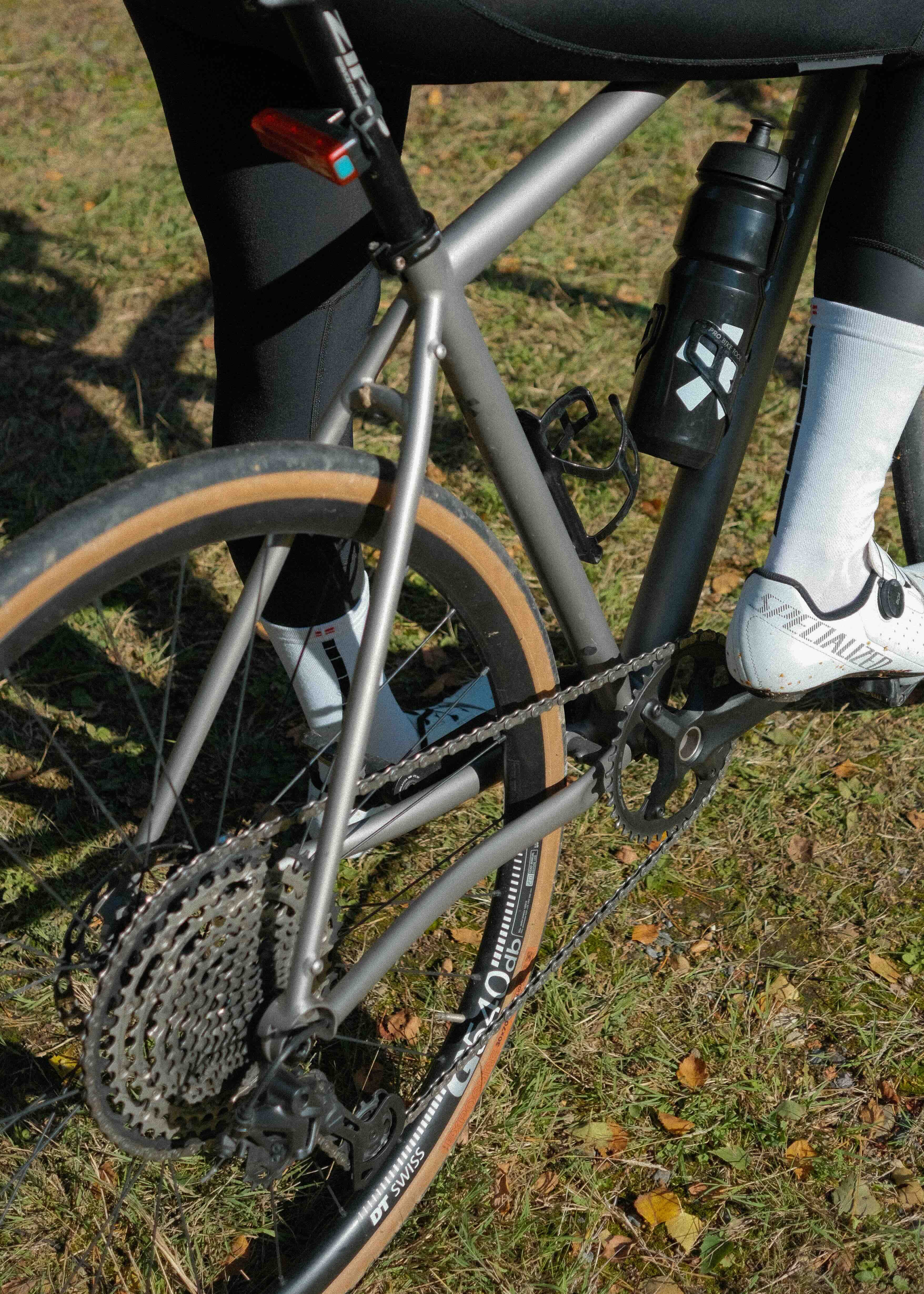 Close-up of a bicycle with a person wearing a black outfit and white shoes on grass.