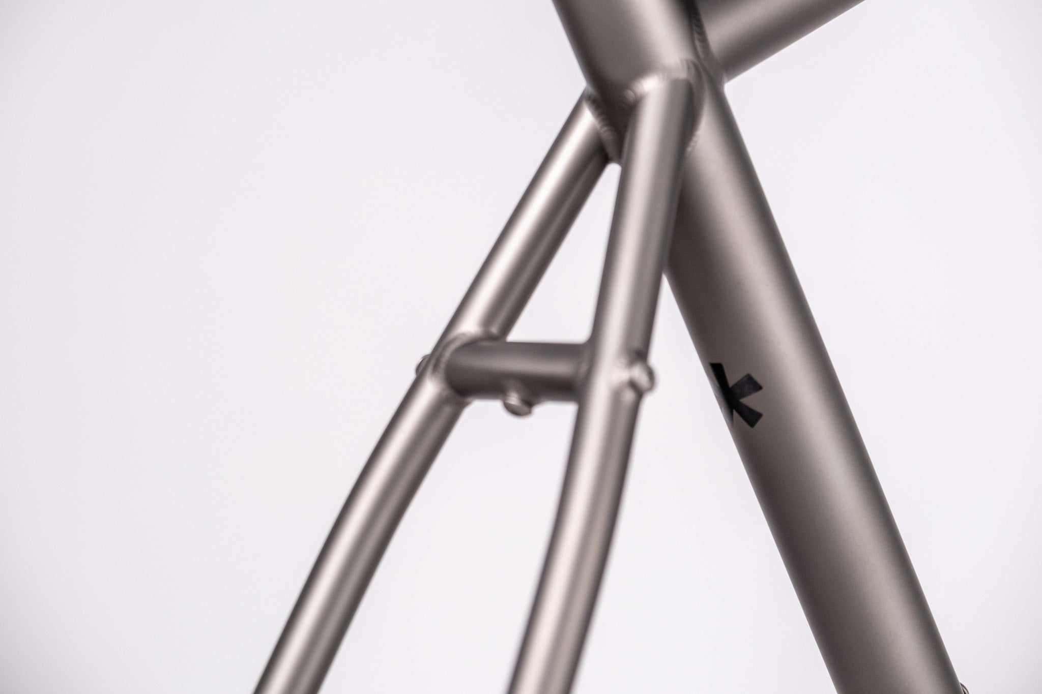 Close-up of a metallic titanium  bicycle frame with a brand logo on a white background