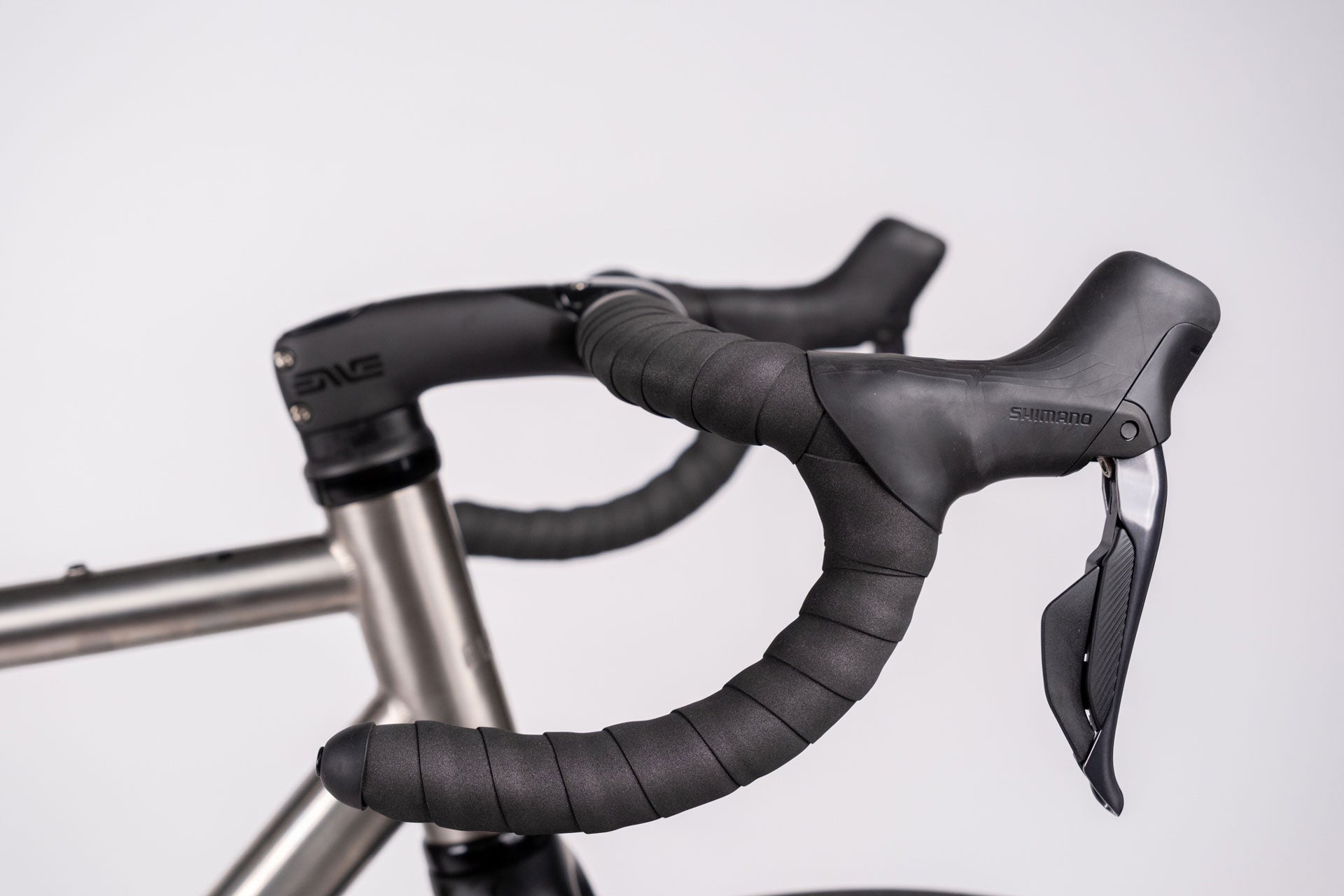 Close-up of a bicycle handlebar with black grips and silver frame on a light gray background