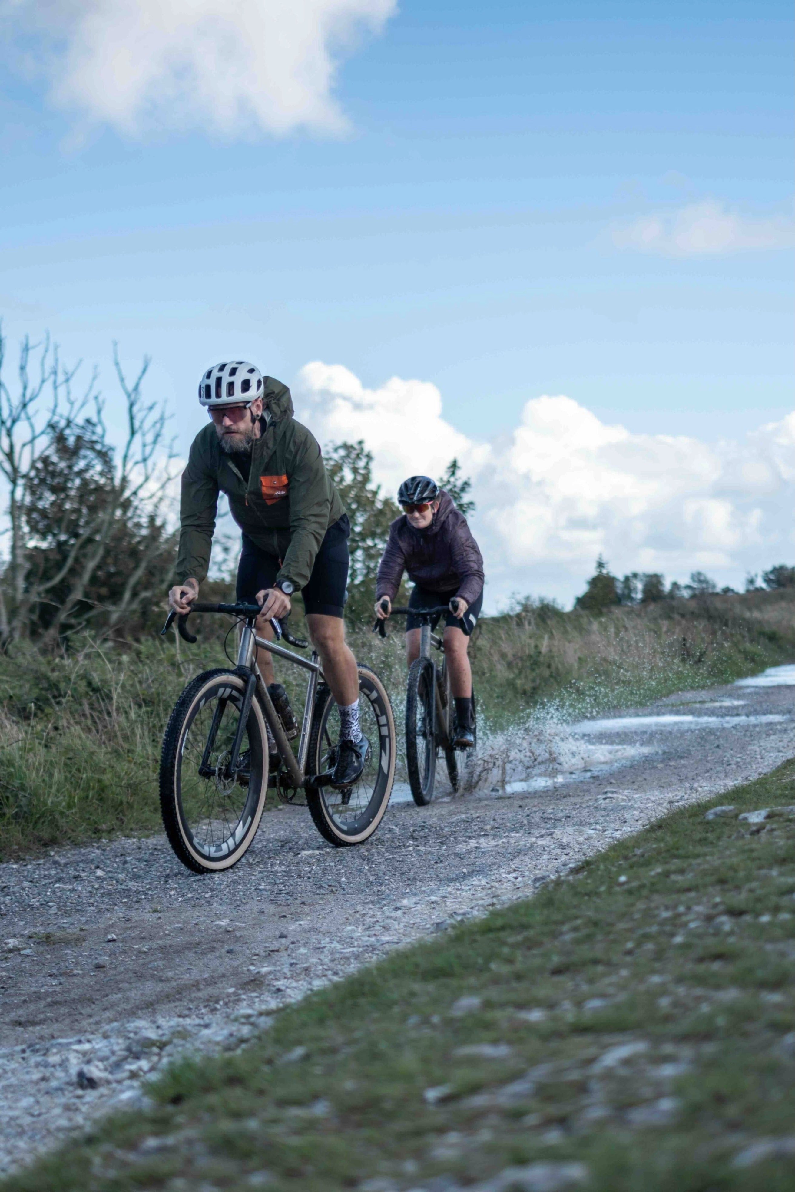 Two cyclists riding on a gravel path with a clear blue sky.