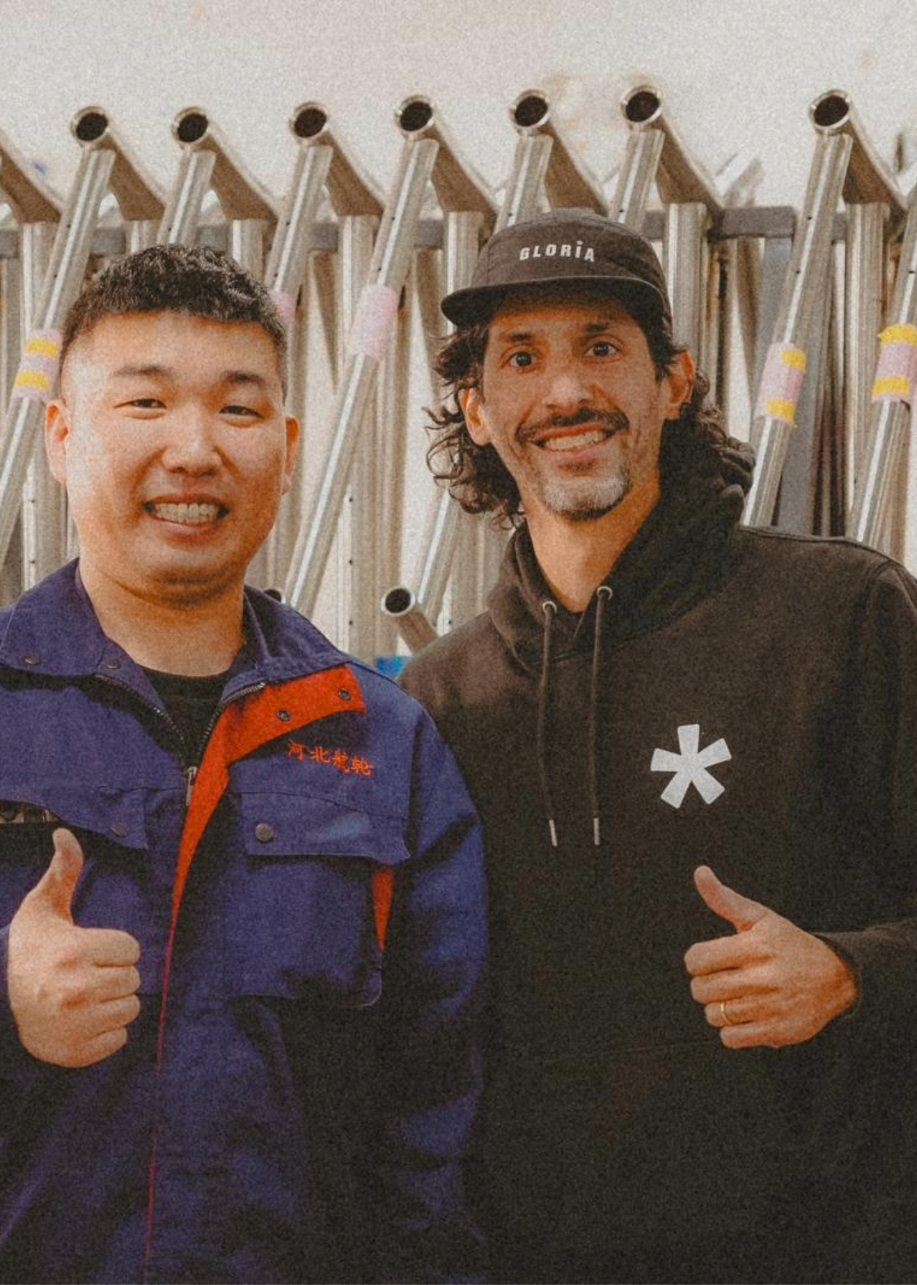 Two men giving thumbs up in front of a titanium bicycle frames