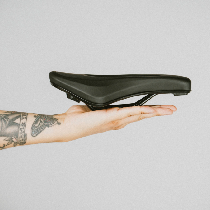 Black bicycle seat held in a hand against a plain background