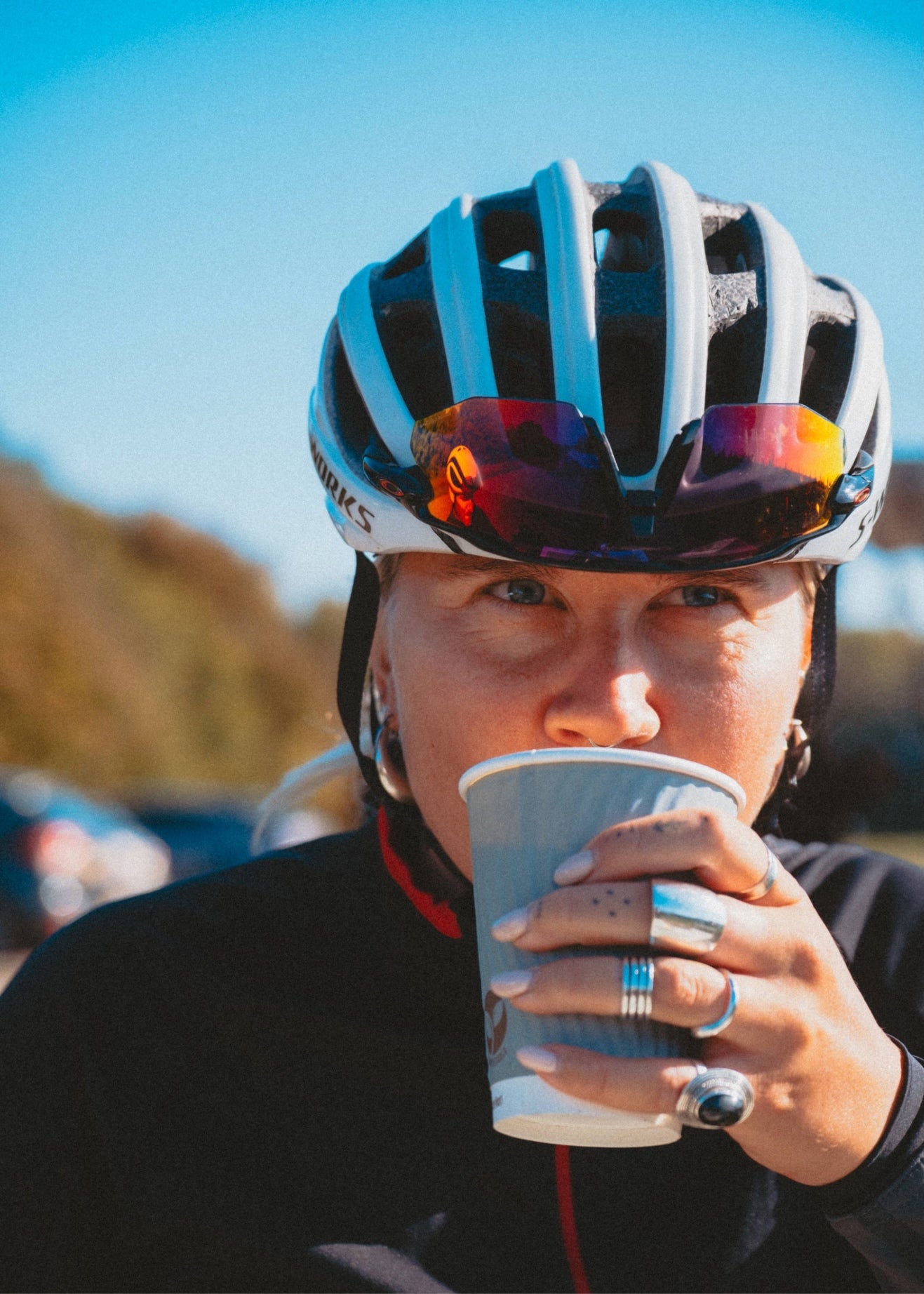 Person wearing a bicycle helmet and drinking from a paper cup outdoors